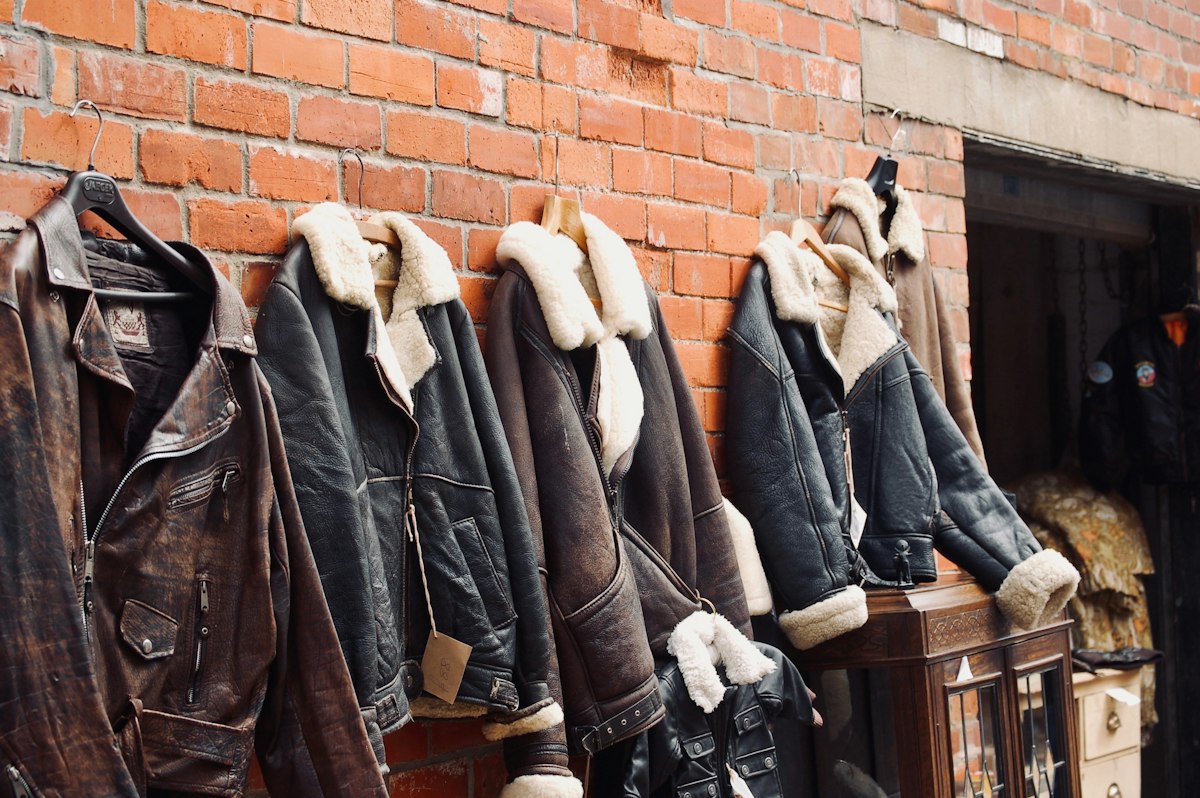 Leather and shearling jackets hanging on a red brick wall outside the workshop door