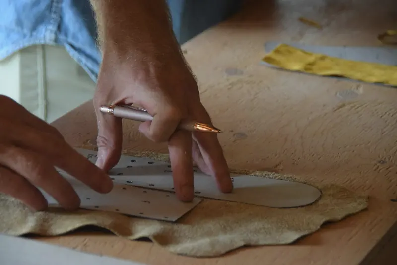Hands marking a leather panel from a paper pattern on a wooden bench