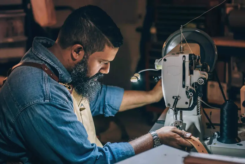 Machinist stitching a leather belt on a walking-foot machine in the workshop