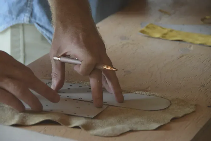 Hands marking a pattern onto pale leather with a pencil