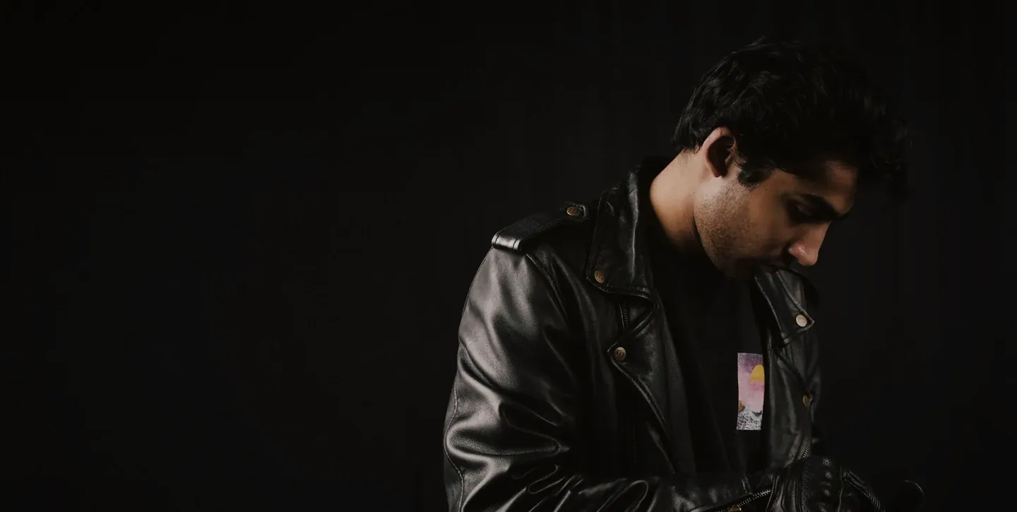 Man in a black leather biker jacket, head bowed, in a dark studio